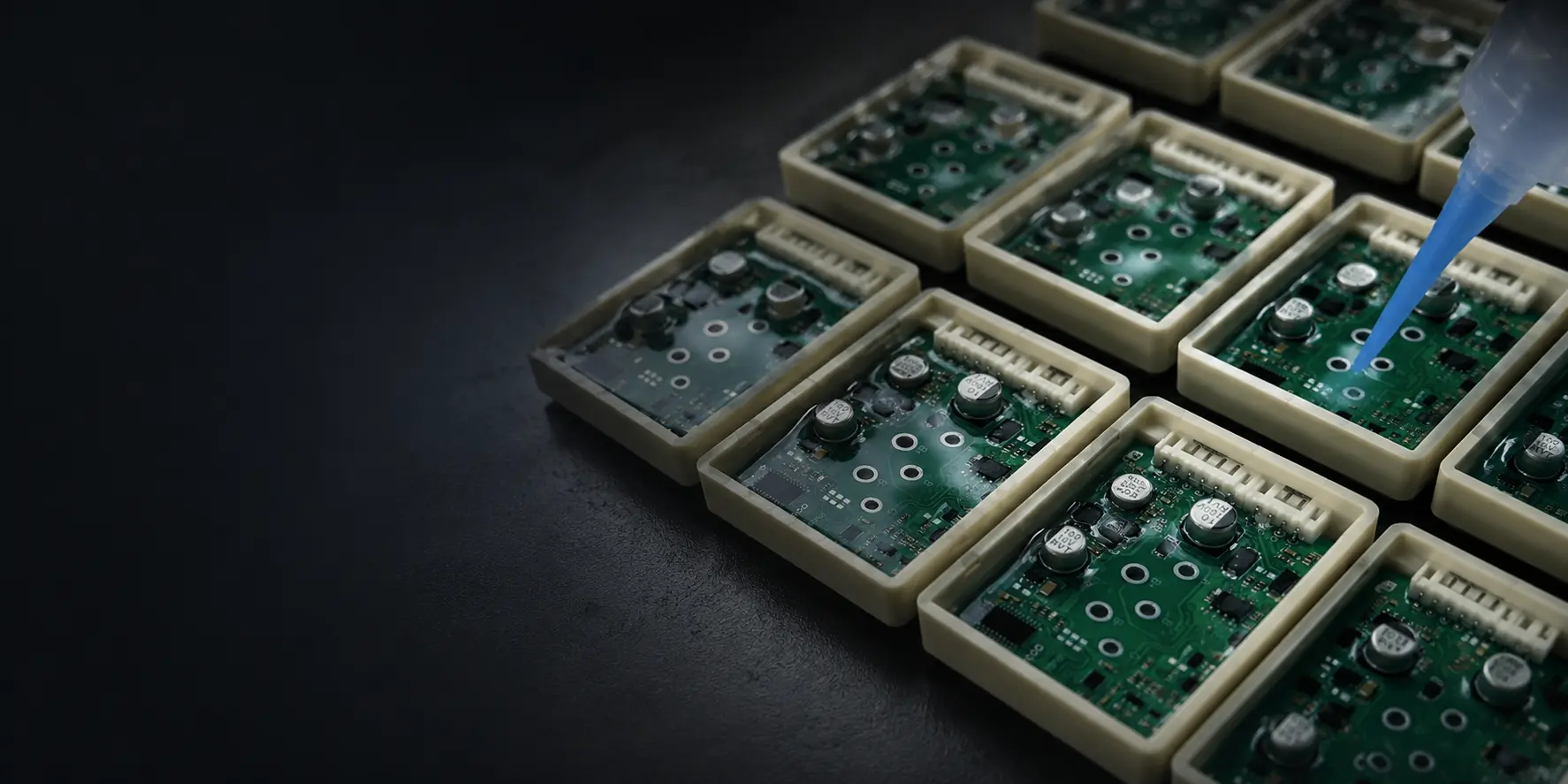 Dispensing needle applying potting compound onto circuit boards seated in plastic housings