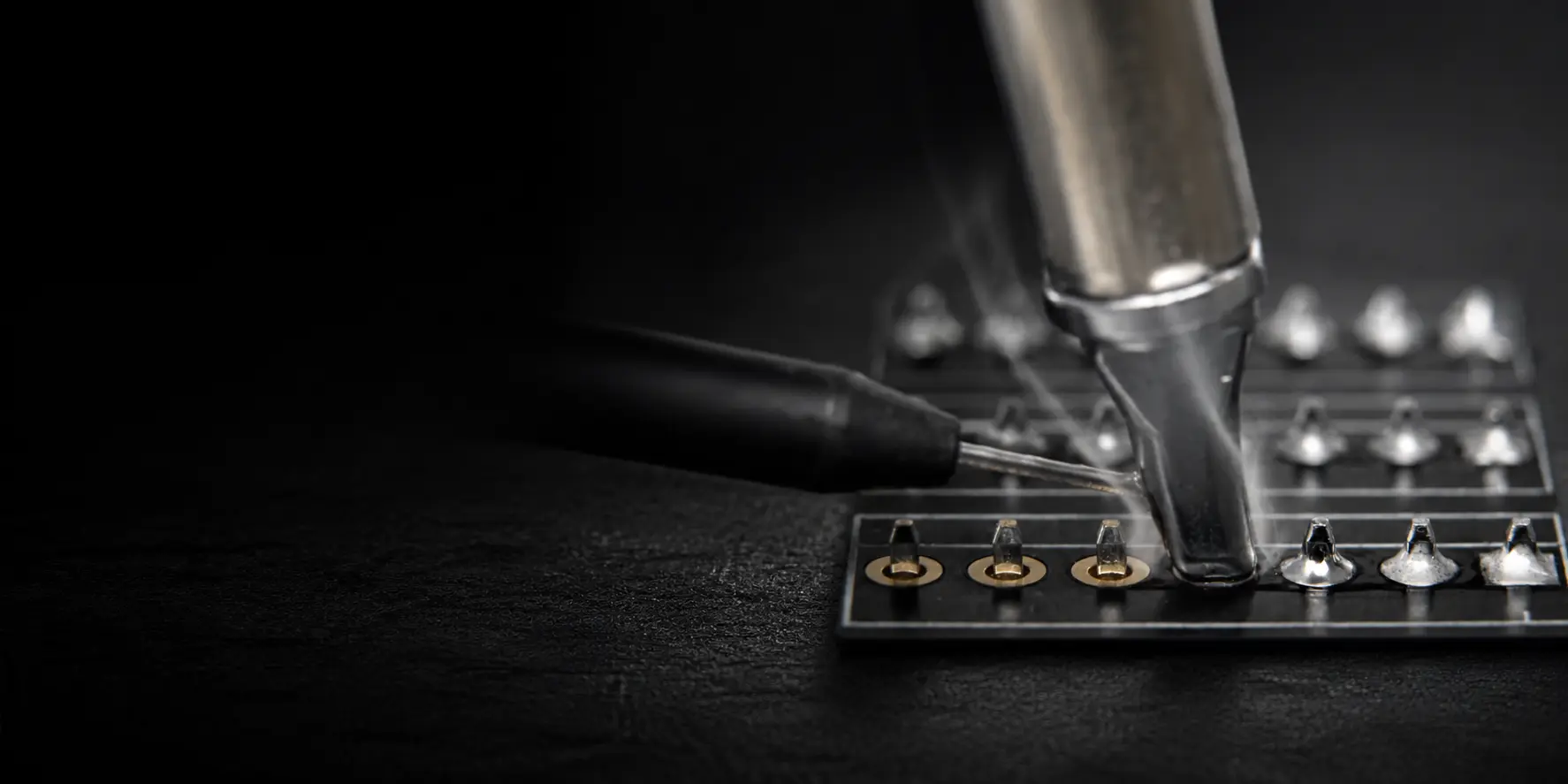 Soldering iron tip and solder wire forming joints on a row of terminal pins on a circuit board
